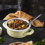 Beef stew in a yellow ceramic pot on a black wooden tabel