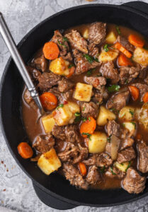 beef stew with carrots, beef and potatoes in a cast iron pot on a table