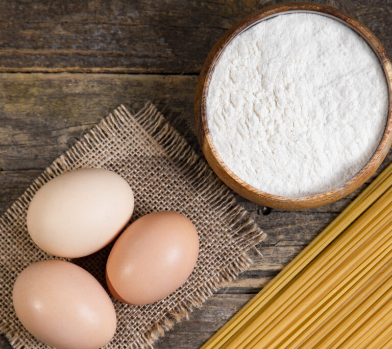 three eggs and a wooden bowl of flour