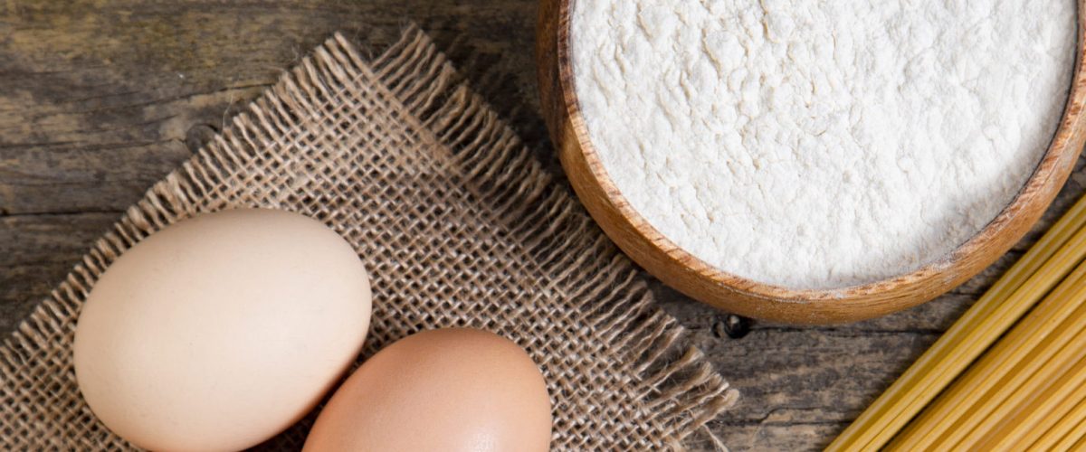 three eggs and a wooden bowl of flour