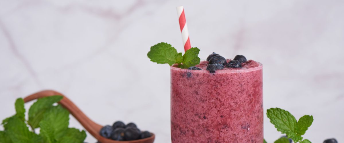 small glass full with rich red blue smoothie topped with blueberries with blueberries sprinkled around on a white background
